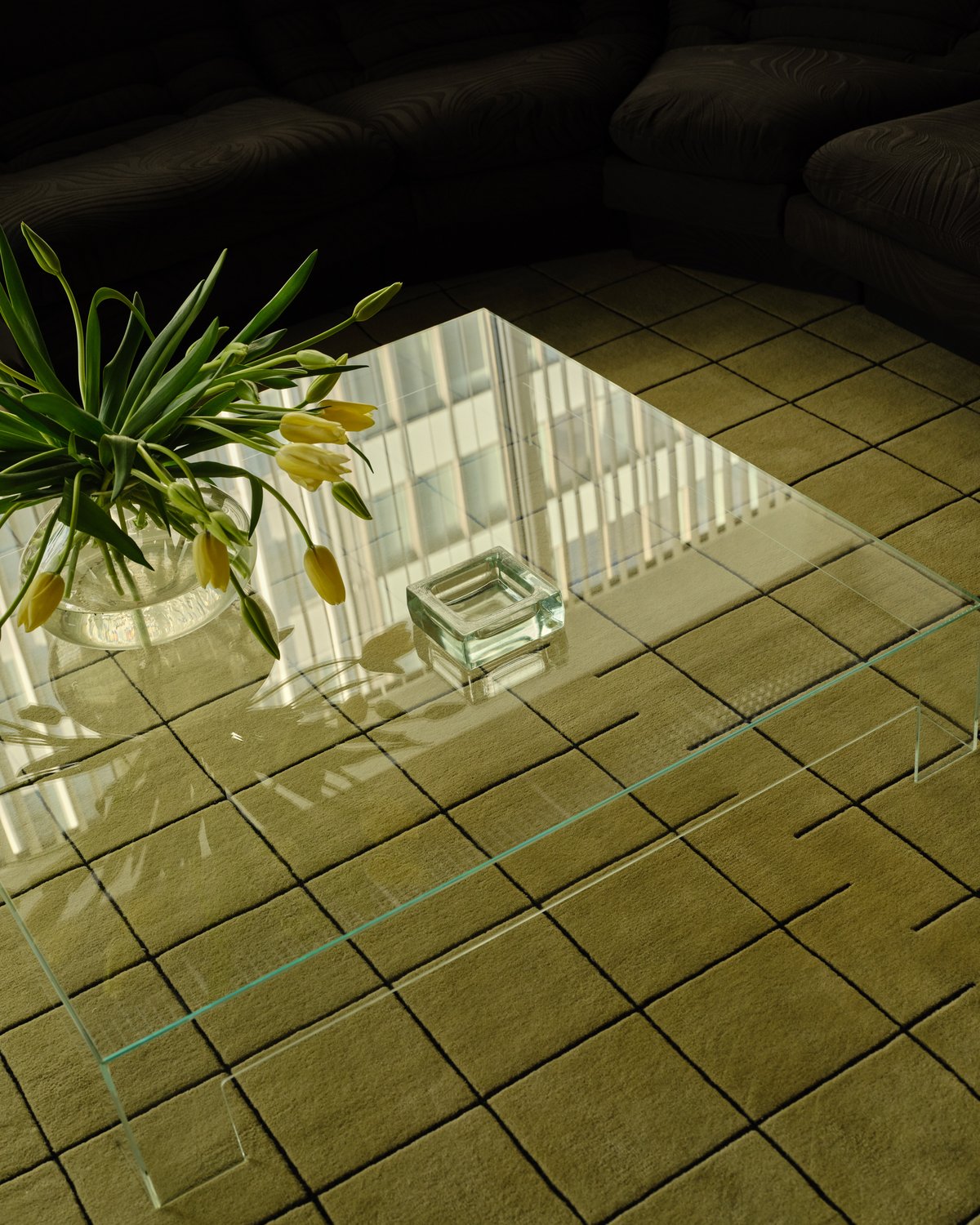 Gros plan du tapis Grid en coloris Pistachio/Black, apportant une structure subtile et de la douceur à un salon moderne et élégant avec des sièges en velours sombre et des accents en verre.