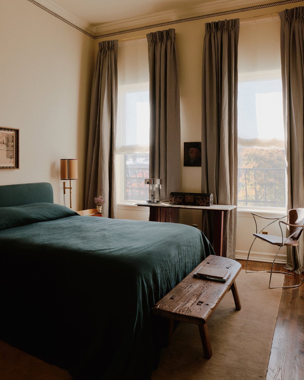 Flauschiger Wollteppich Grand in der Farbe Chestnut abgebildet in einem Schlafzimmer mit hohen Fenstern, die mit grauen Vorhängen bedeckt sind und Licht auf ein großes Bett in Teal filtern.