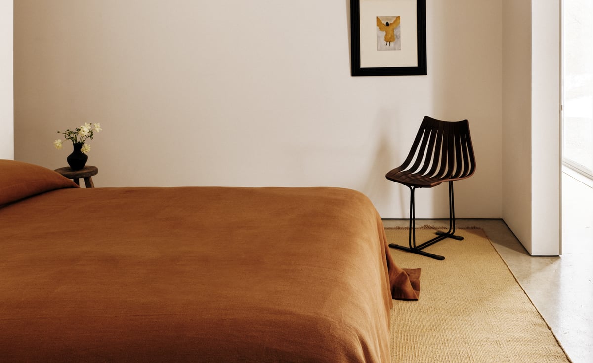 Studio Linen Bedspread in Brandy displayed on a bed, highlighting its natural linen texture and rich, earthy tone. A Desert rug in Straw is placed underneath.