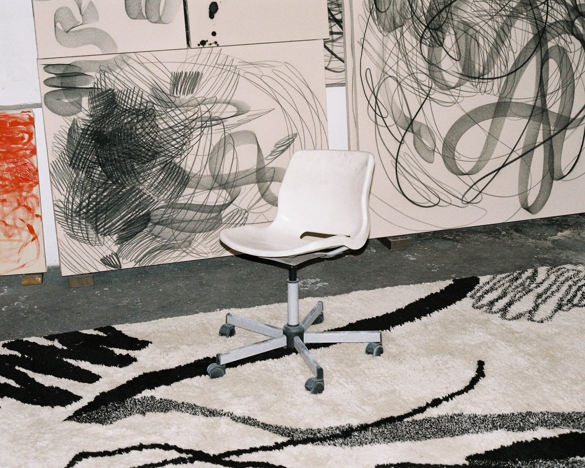 1212/21 Aythamy Armas rug under a chair with similarly patterned artworks in the background.