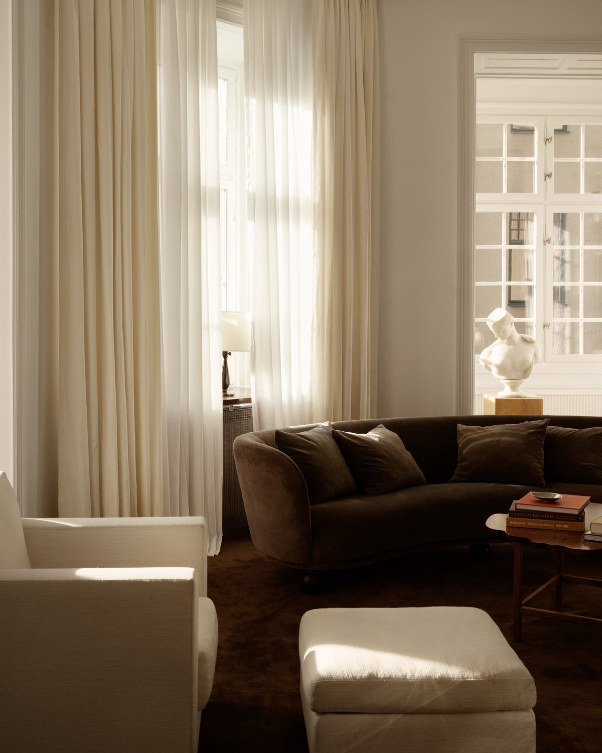 Nordic Knots Vorhänge aus transparentem Stoff, abgebildet hängend in einem modernen Wohnzimmer mit braunem Sofa und weißem Sessel.