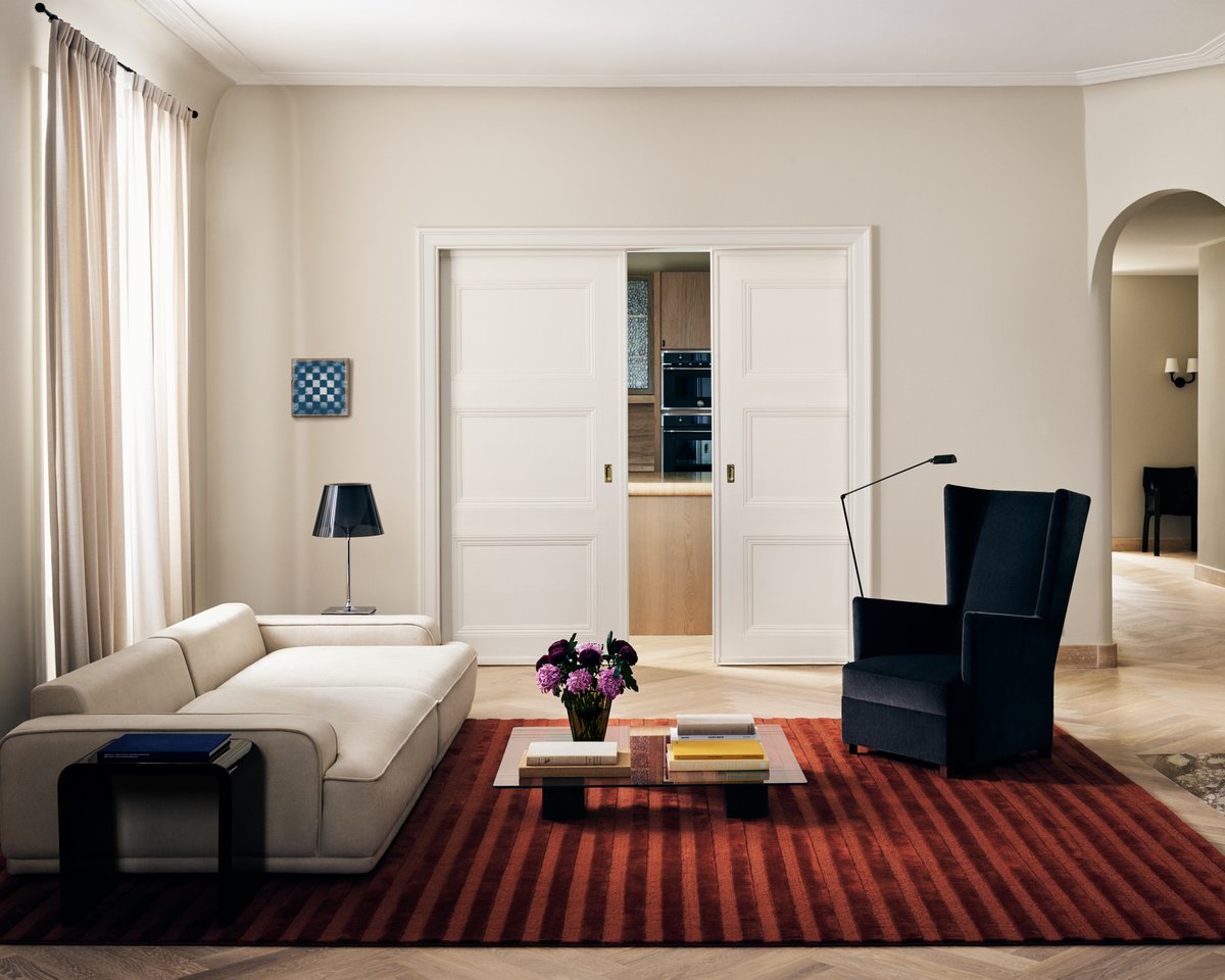 Plush wool rug Park 03 in Burgundy photographed in a brightly lit Stockholm apartment with a large navy armchair and white sofa.