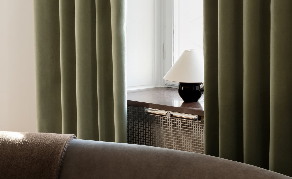 Gardinen The Velvet – Olive Green ramar in ett ljust fönster, med len sammets­textur som tillför värme och lugn till rummet.