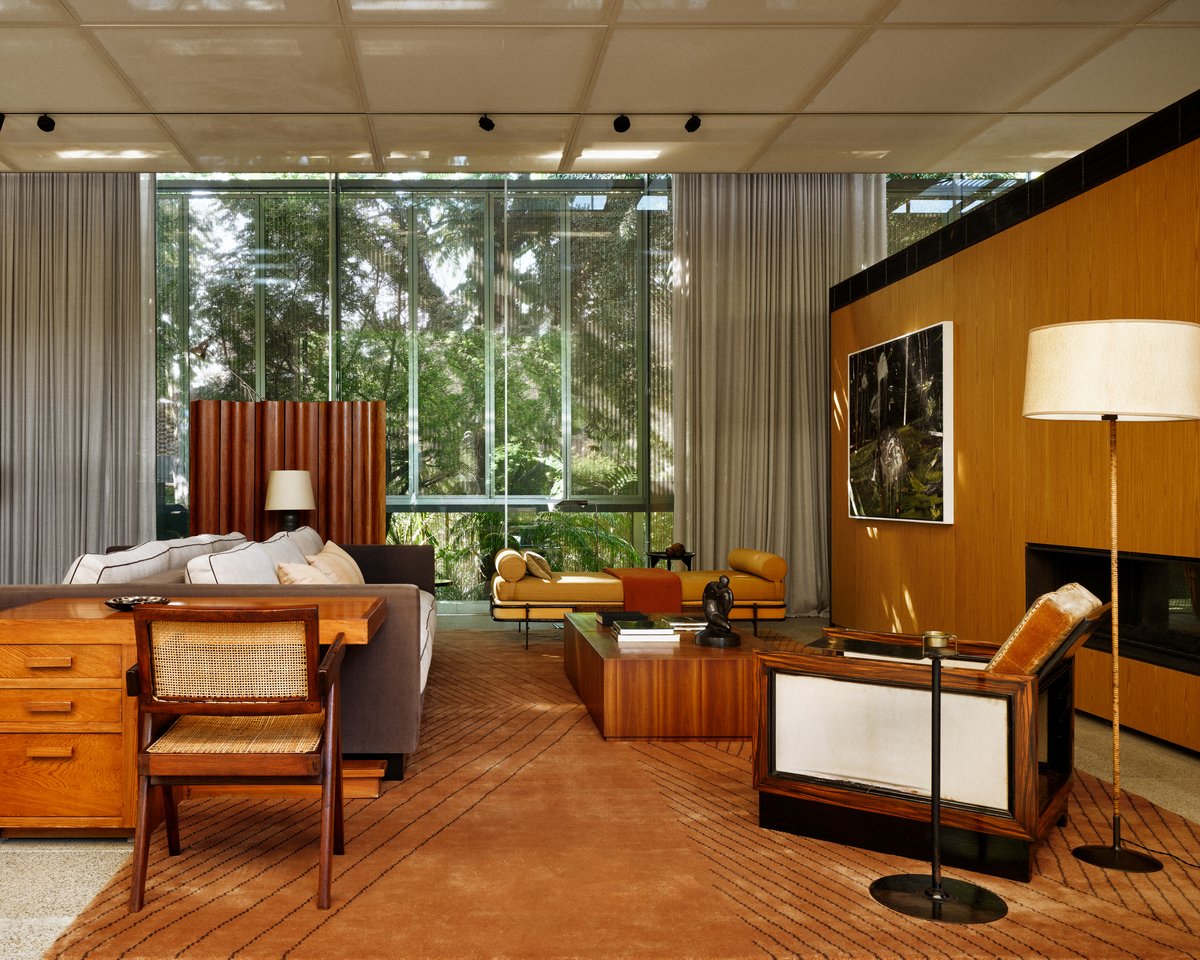 The Indore rug in Terracotta, styled in a São Paulo living room with large glass windows, mid-century furniture, warm wood paneling, and soft natural light.