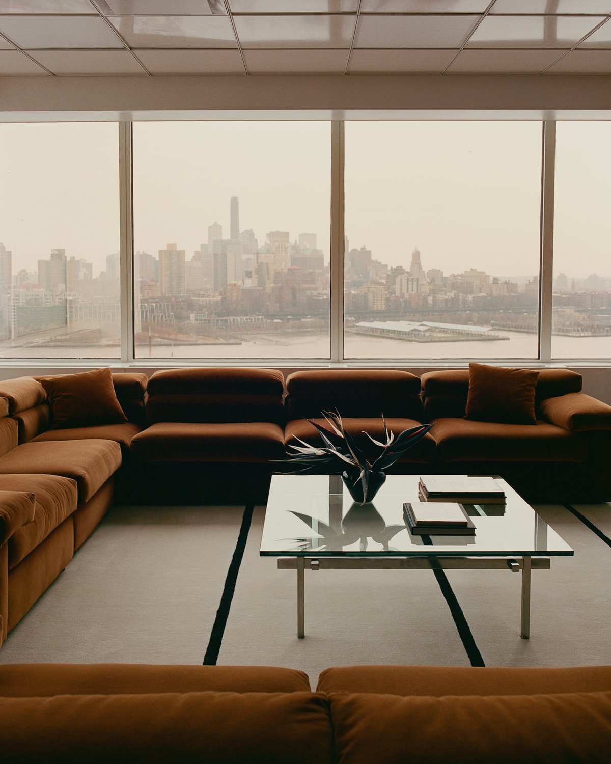 Le tapis Norr Mälarstrand 01 en Dusty White/Black présenté dans un salon moderne et élégant d’un gratte-ciel à New York, associé à un canapé en velours marron et une table basse en verre.