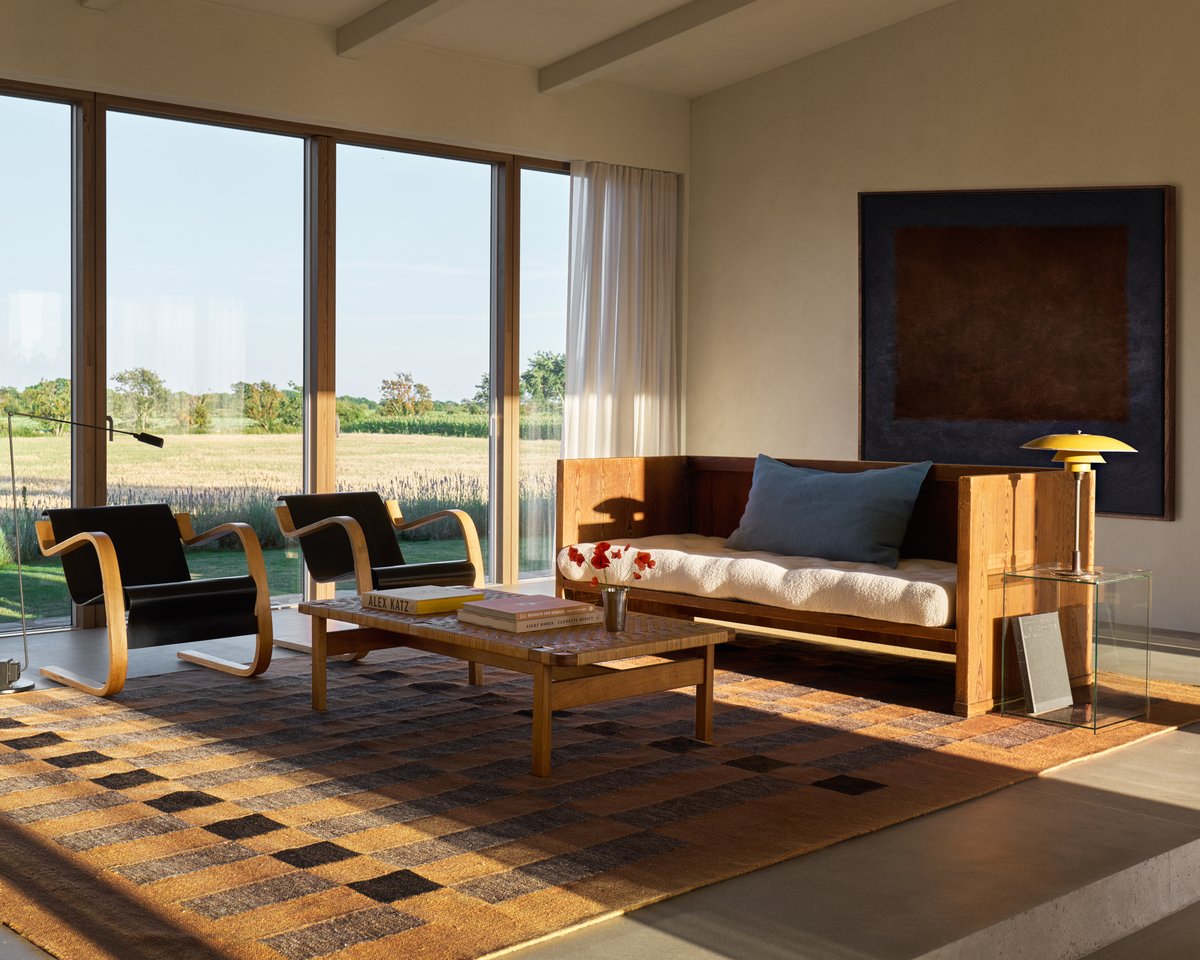 A spacious modern living room with Tradition 02 in Orange, where the rug anchors wooden lounge furniture, with large windows framing lush nature.