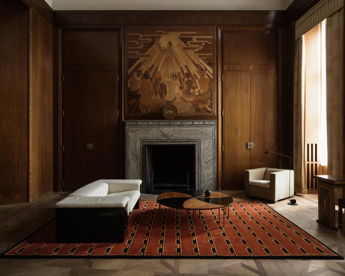 Plush wool rug Gild 02 pictured in an elegant living room with tall wooden walls and a grand marble fireplace.