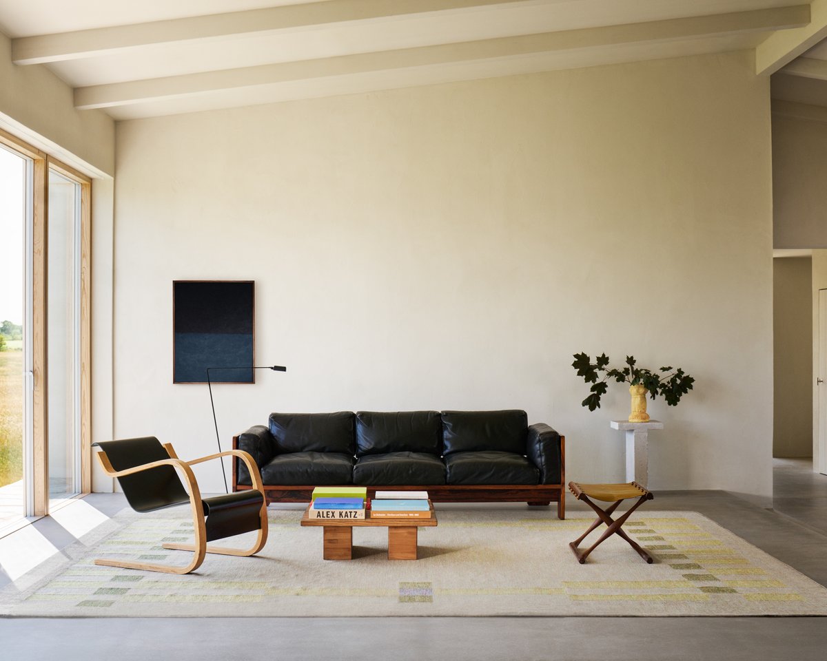 A wide shot of a living room with Tradition 02 in Green, surrounded by black lounge furniture and a wooden table, blending modern and organic textures.