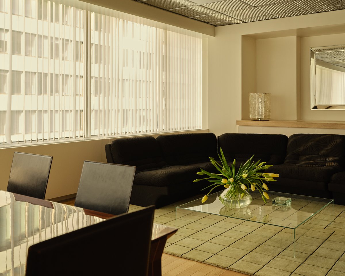 Le tapis Grid en Pistachio/Black apporte une structure subtile et de la douceur à un salon moderne avec des sièges en velours foncé, des accents en verre et une lumière tamisée de la ville filtrée par des stores verticaux.