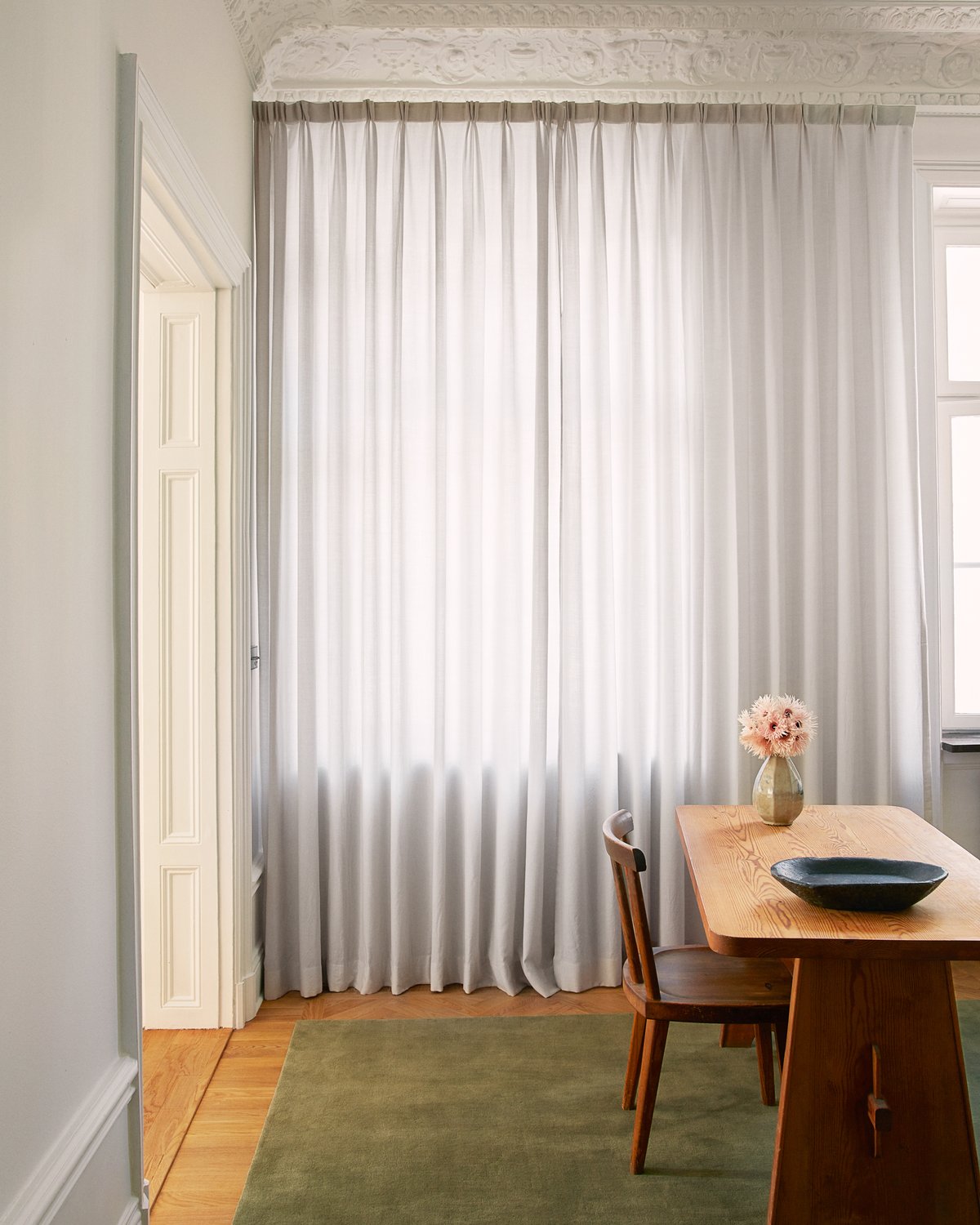 Wollvorhang The Grand in der Farbe Soft Gray, präsentiert in einem Büro mit Holzelementen im Interieur und dem Plüschwollteppich Grand in Moss.