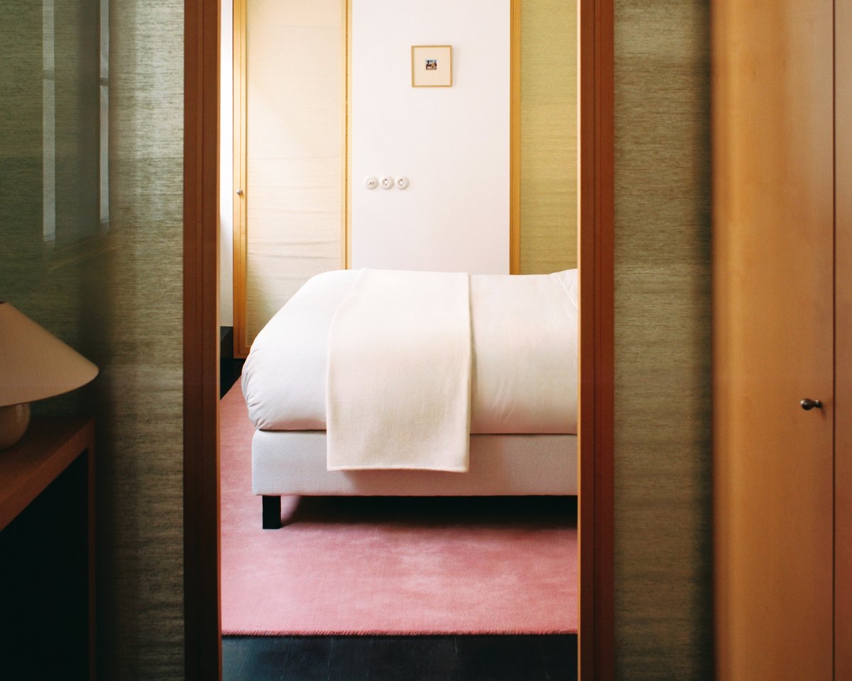 Grand in Sakura Pink, photographed from the doorway in a bedroom beneath a bed with crisp white bedding.