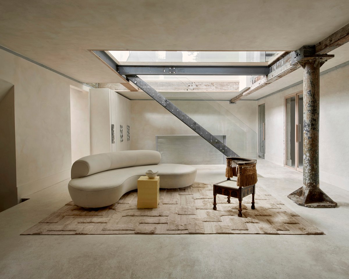 Boho rug in Sand Mix in an industrial space underneath a curved cream sofa and yellow side table.