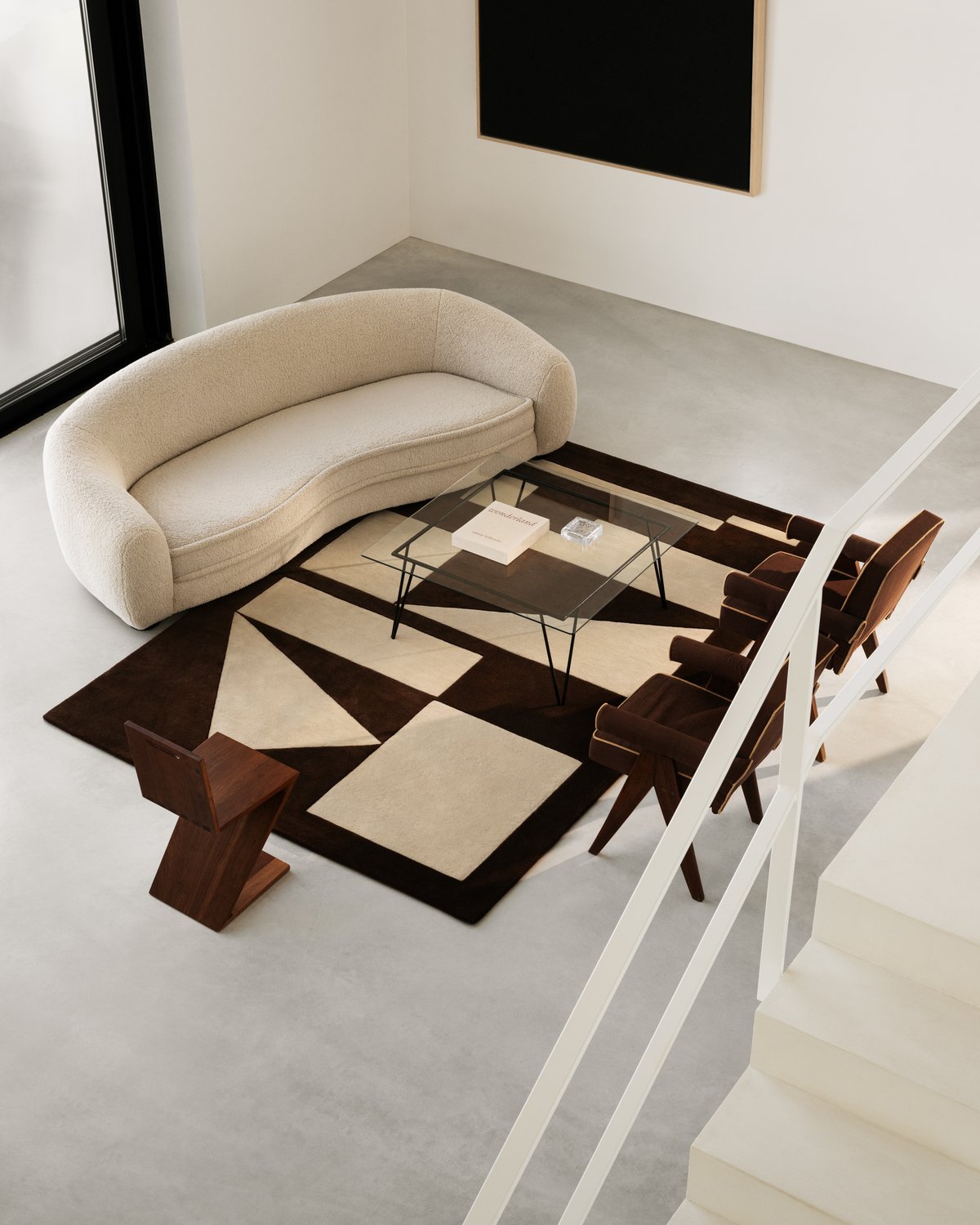 Tapis en laine moelleux Untitled 03 photographié depuis un escalier, sous une table basse en verre et des meubles design artistiques aux tons doux.