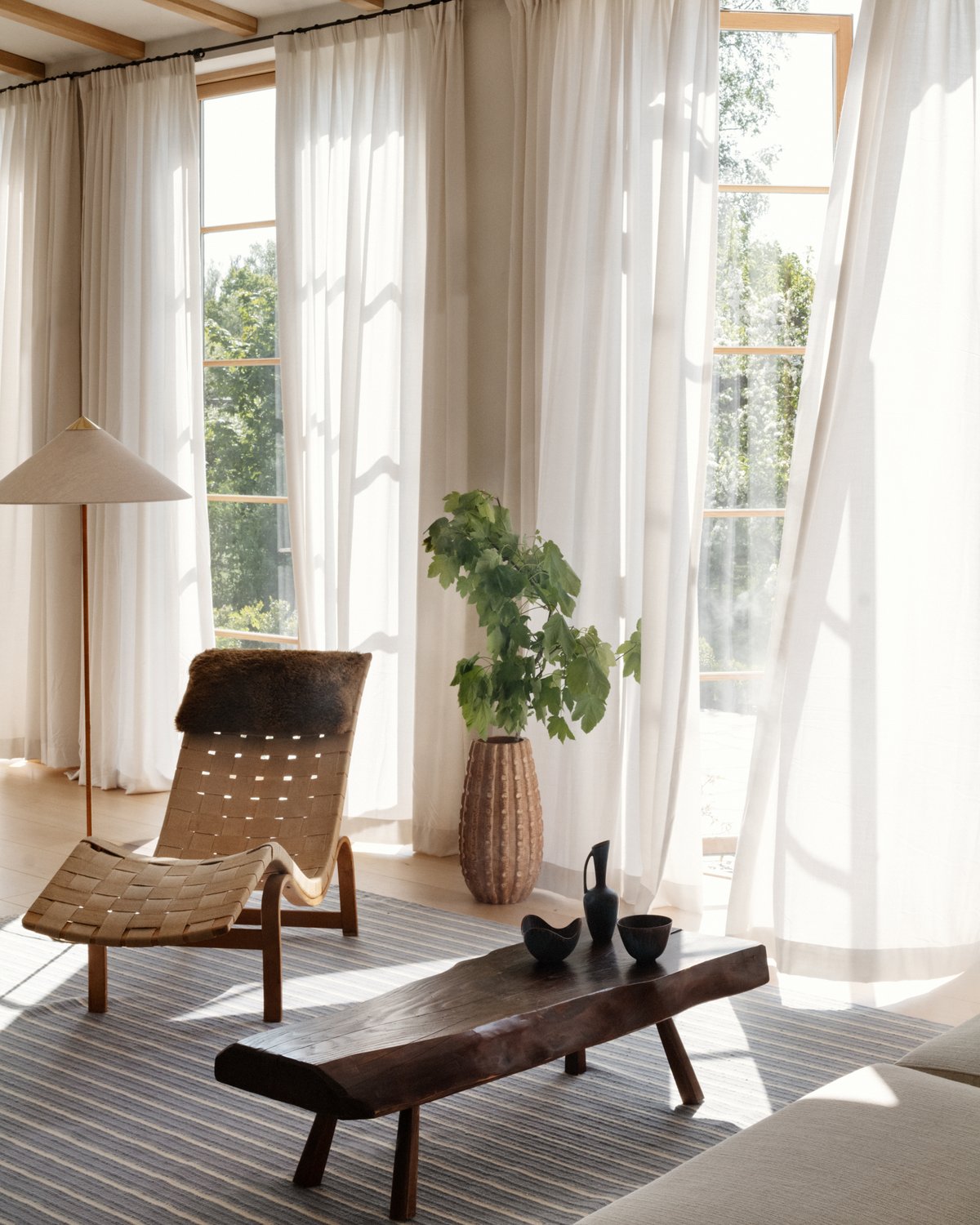 Shirt Stripes in Blue in a bright lounge with white sheer curtains, a rattan chaise lounge, a green plant, and a wooden bench.