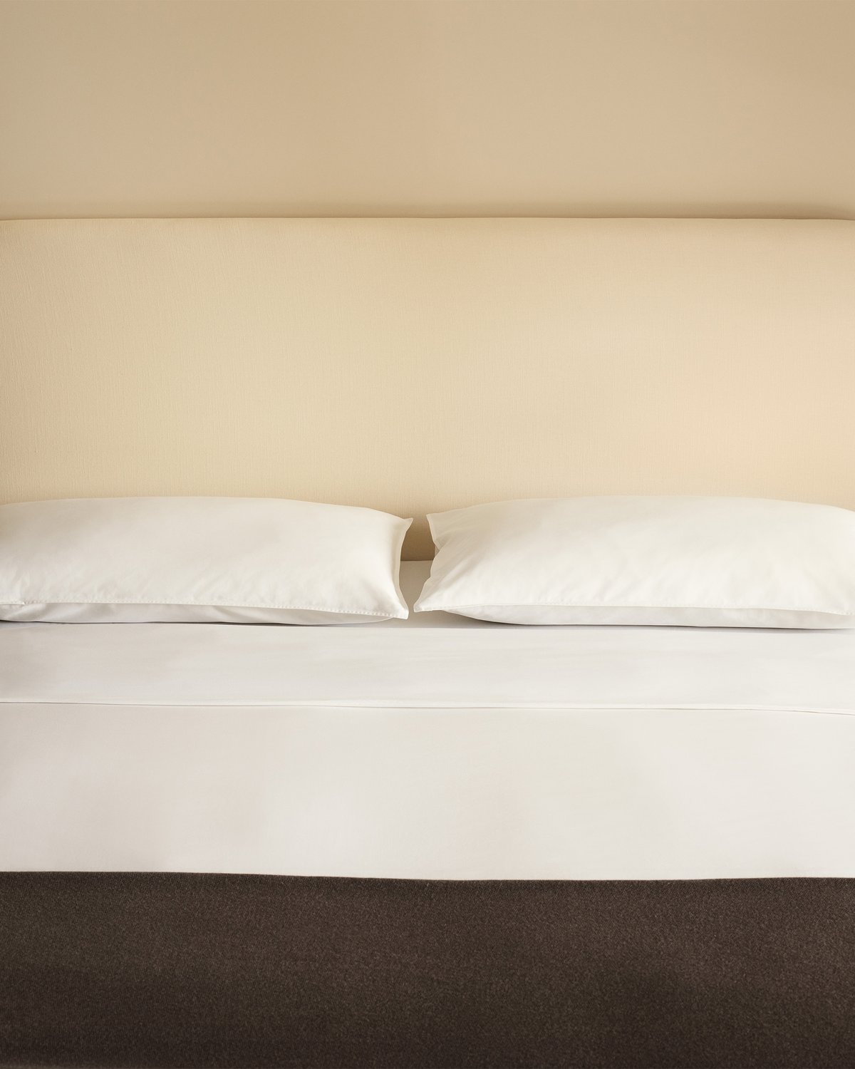Crisp white bedding styled with the Signature Headboard in Warm White and a Heritage throw in Taupe, photographed straight on.