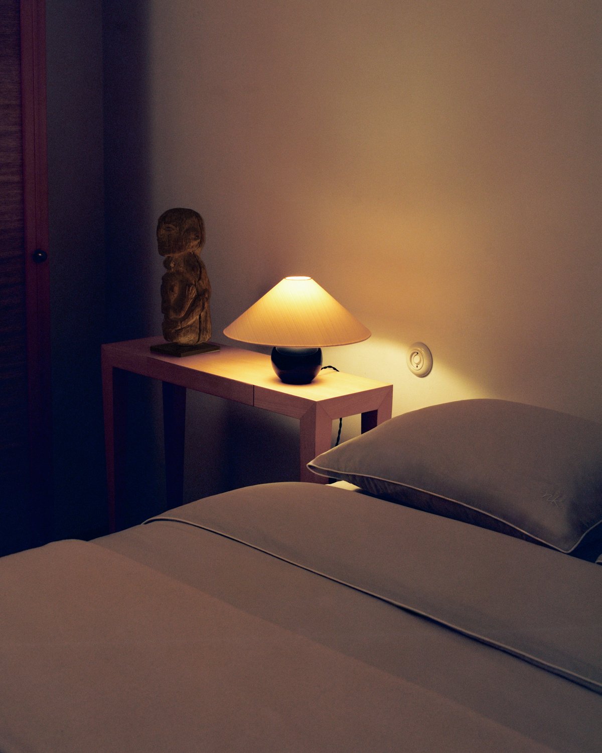 Percale bedding, photographed in a softly lit bedroom with a bedside table and lamp.