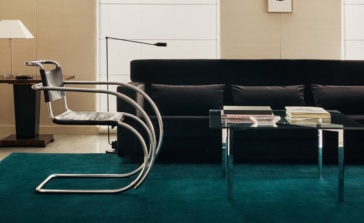 Grand in Emerald Green, photographed in a sleek modern lounge beneath a black sofa, styled with chrome details and a glass coffee table for a sharp, cinematic mood.