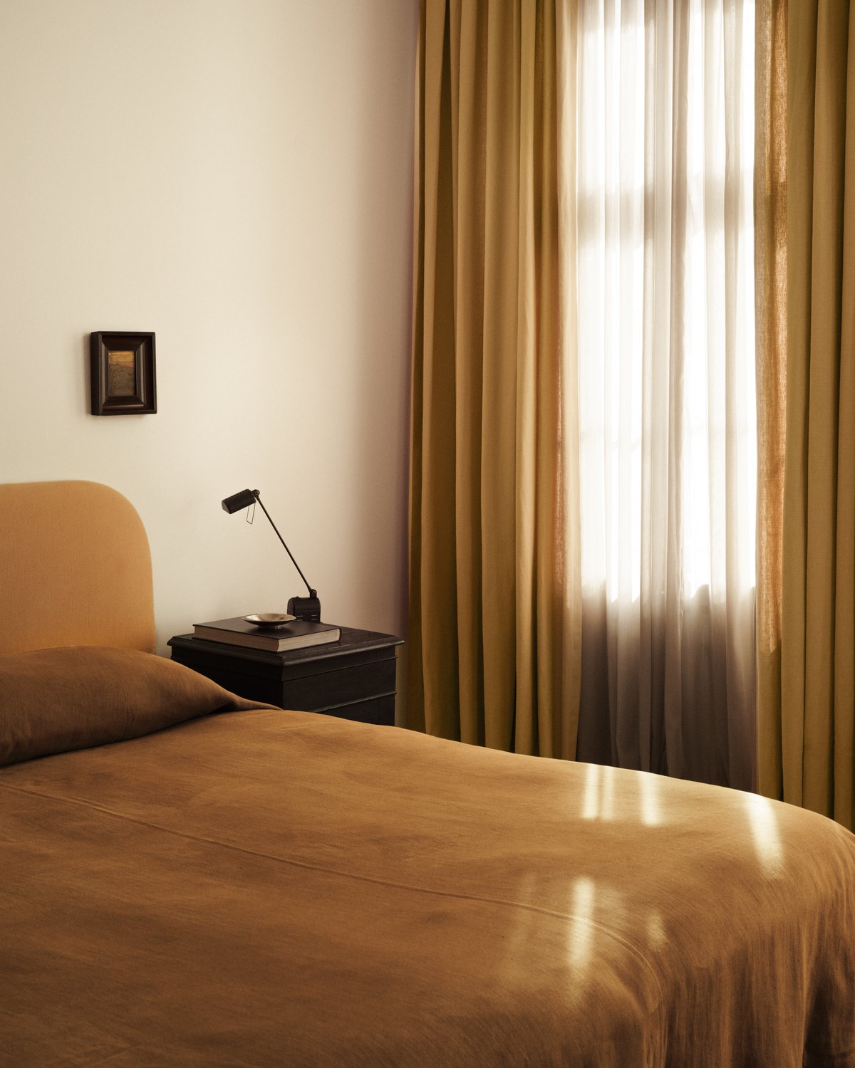 Nordic Knots The Sheer-gardiner fotograferade med solljus som strömmar in genom ett fönster och faller över en rostorangefärgad säng.