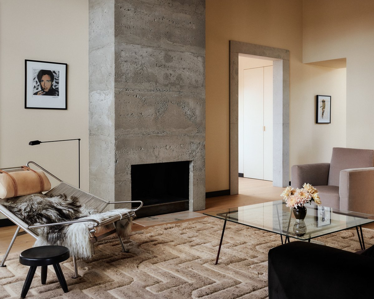 The Boho 02 – Taupe Mix rug in a warm living room with a concrete fireplace and modern furniture. Styled with a glass coffee table, lounge chair, and neutral tones.