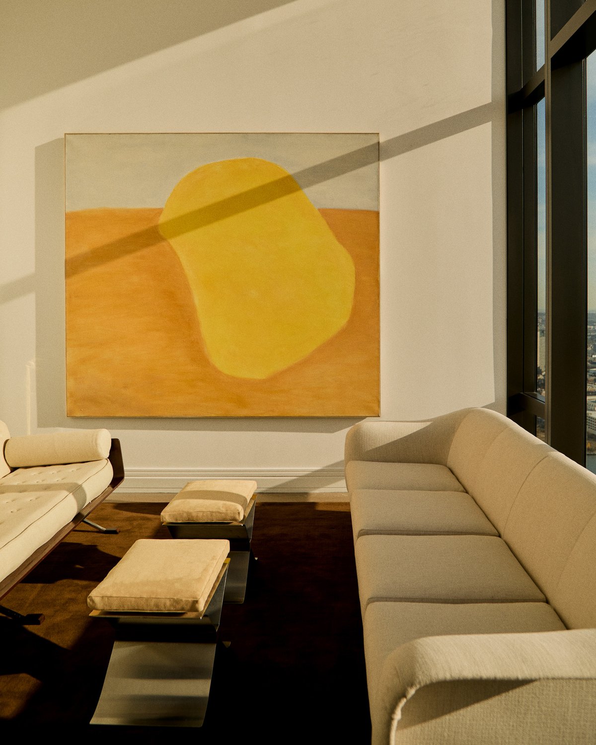 Grand in Walnut, photographed in a sunlit living room between cream sofas and low ottomans.
