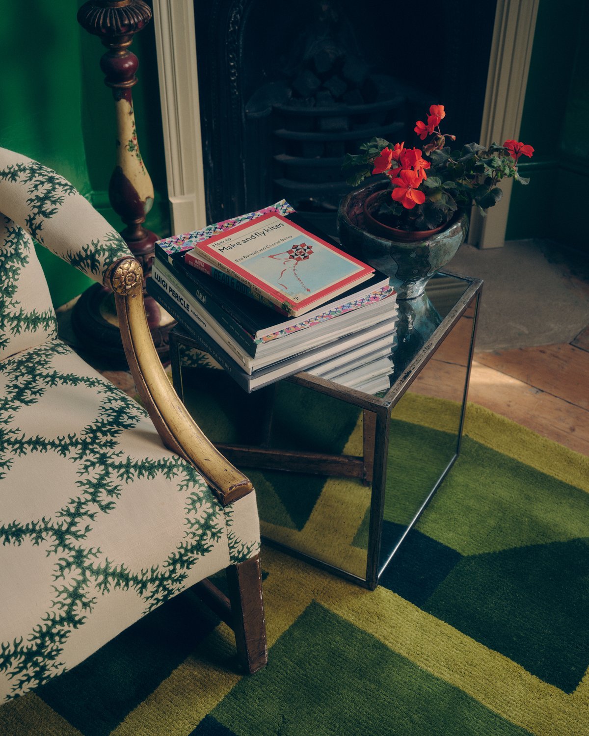 Närbild på den mjuka ullmattan Garden Maze i grönt tillsammans med en fåtölj och en bokstapel på ett litet spegelbord.