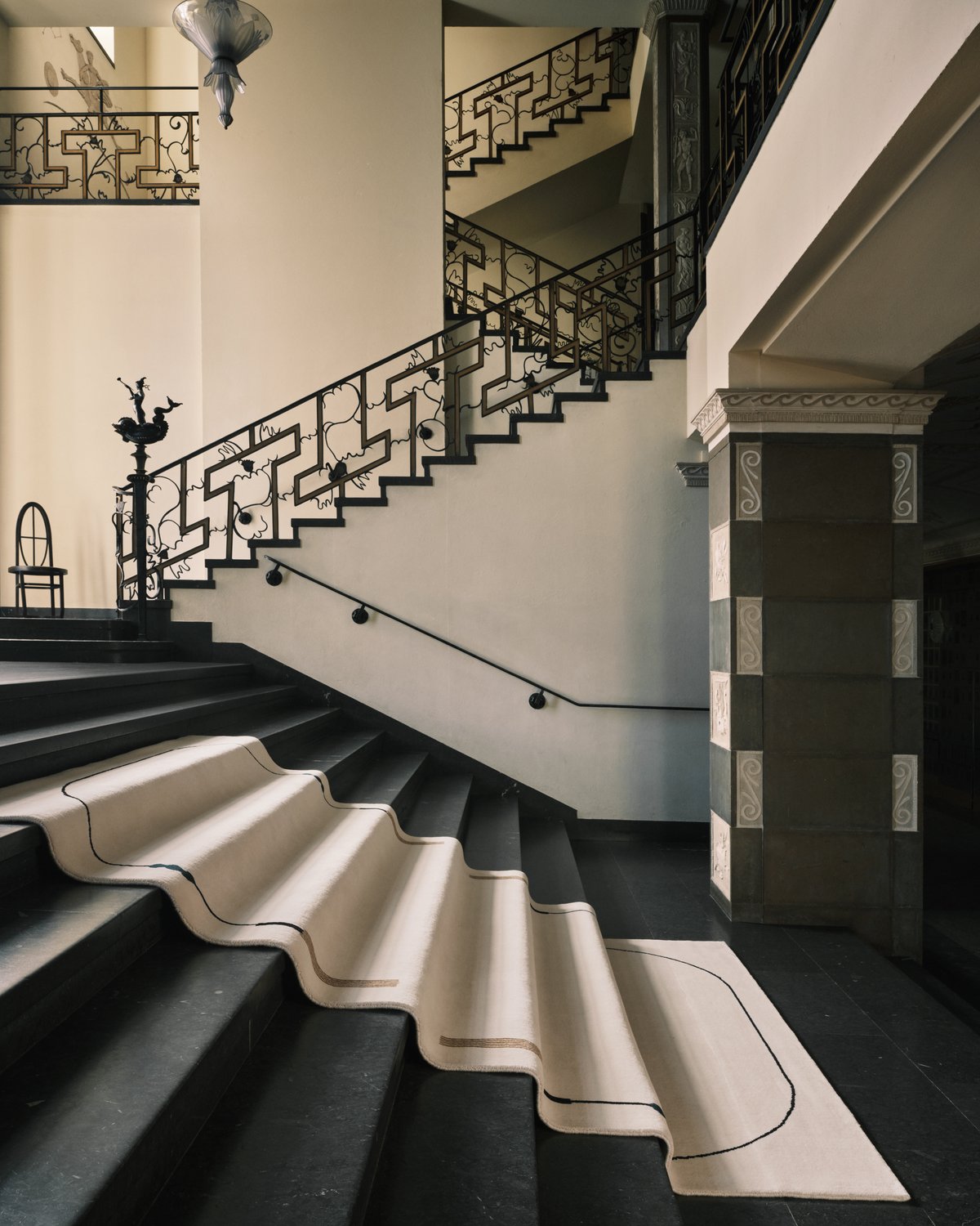 Grace 02 – Tassel — displayed on the grand staircase of Stockholm Concert Hall. The handwoven cream rug features curved black lines and tassel motifs in a balanced, symmetrical composition.