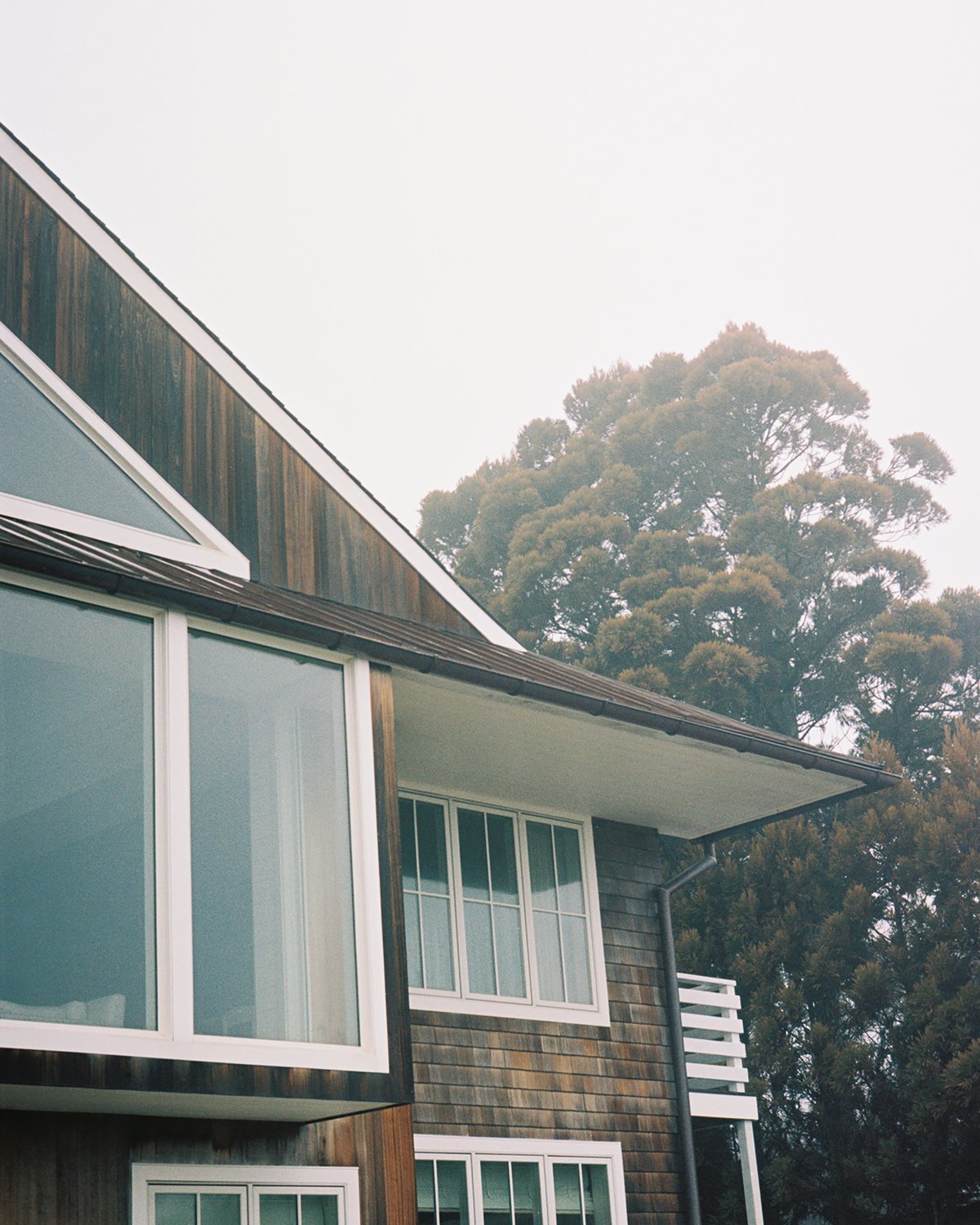 A wooden house with white features pictured during a foggy morning in a green landscape.