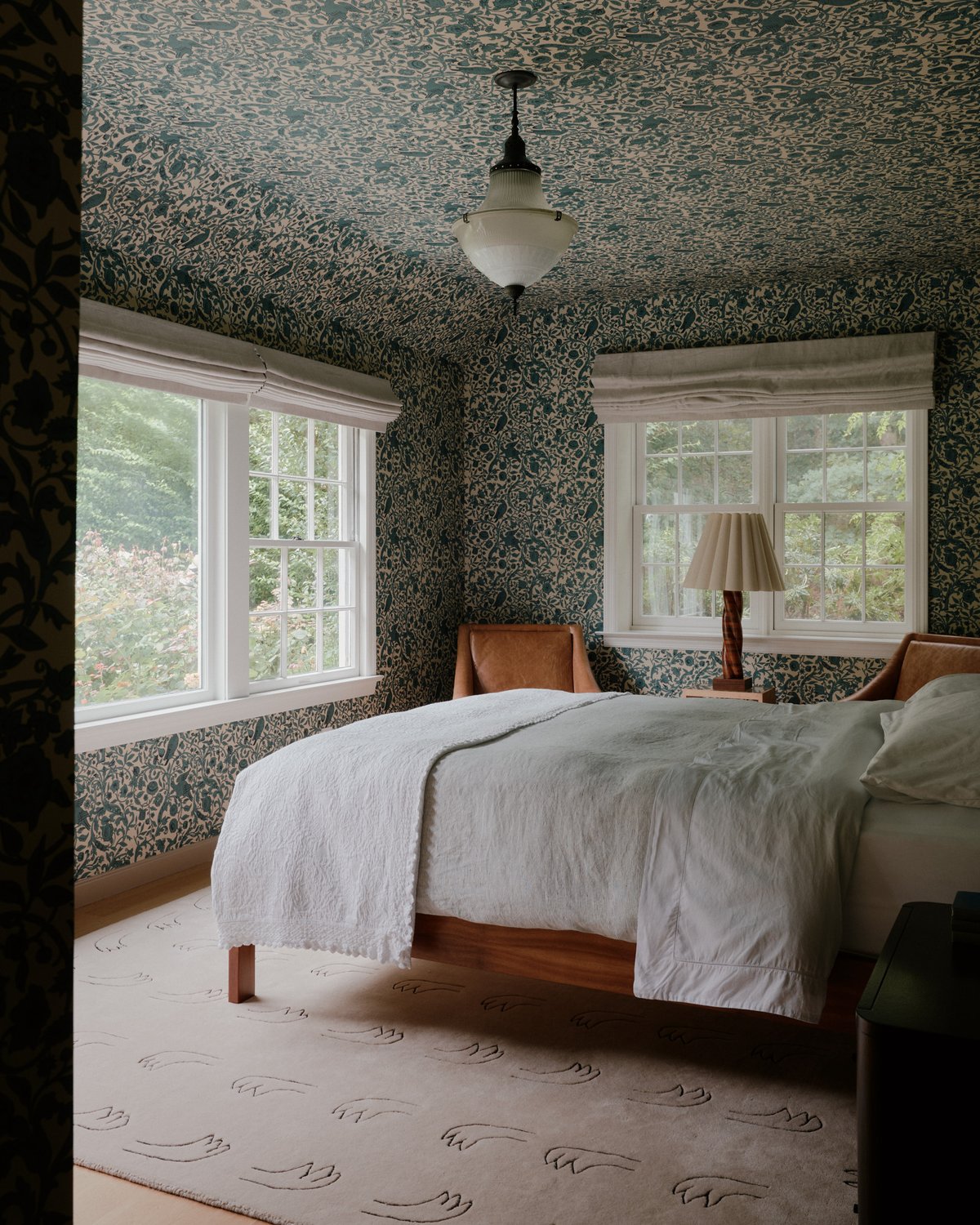 Teppich All Hands in Beige, unter einem Bett inszeniert, zeigt einen weichen Beigeton mit glatter Oberfläche und einem dezenten, wiederholten Handmotiv.