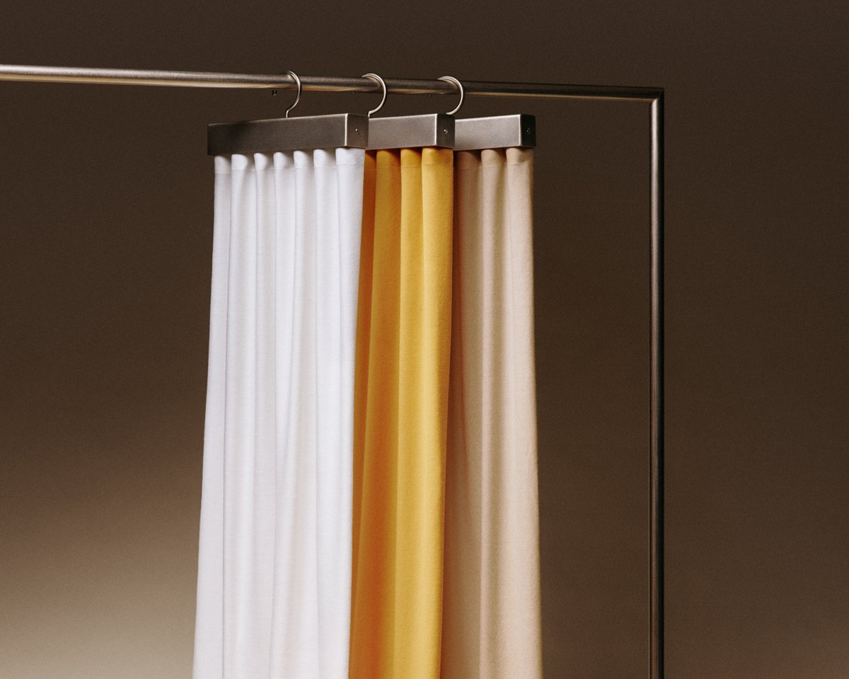 The Grand wool curtains in Perfect White, Leo and Pale sand hanging on a rack.