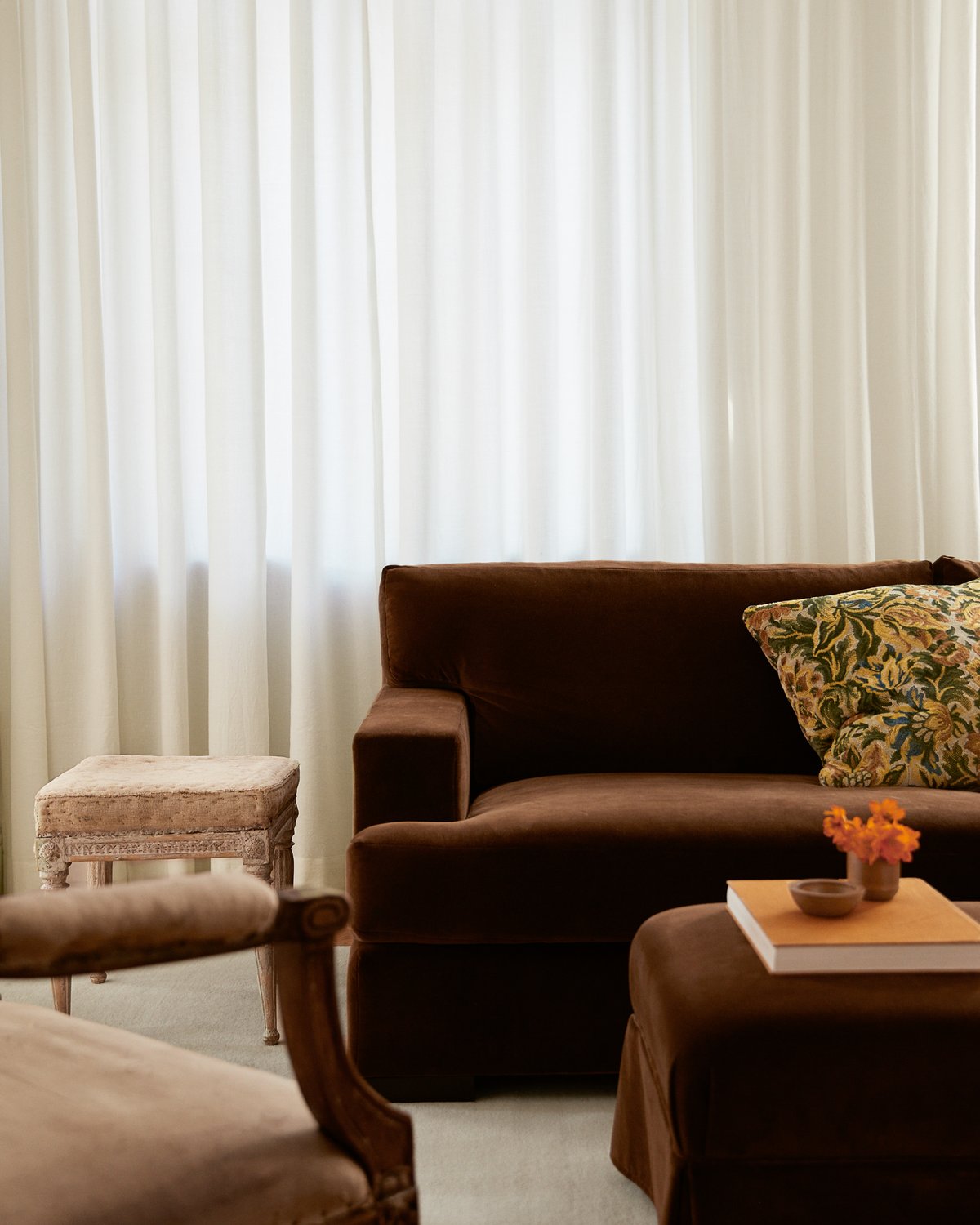 The Grand Vorhänge in Perfect White, fotografiert im weichen Tageslicht hinter einem braunen Sofa mit gemustertem Kissen.