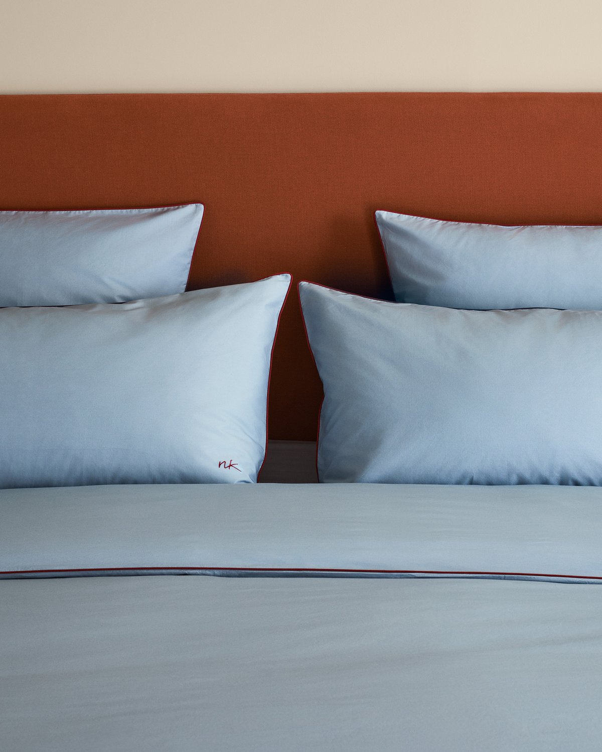 Percale Bedding in Shirt Blue/Red styled with the Signature Headboard in Burnt Red, creating a calm, graphic bedroom composition.
