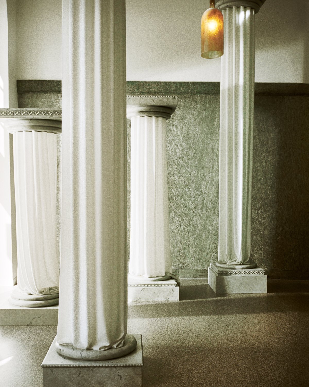 The Grand curtains on an ancient greek style pillar in the Stockholm Flagship with the light shining in through the windows onto the green marble interior.