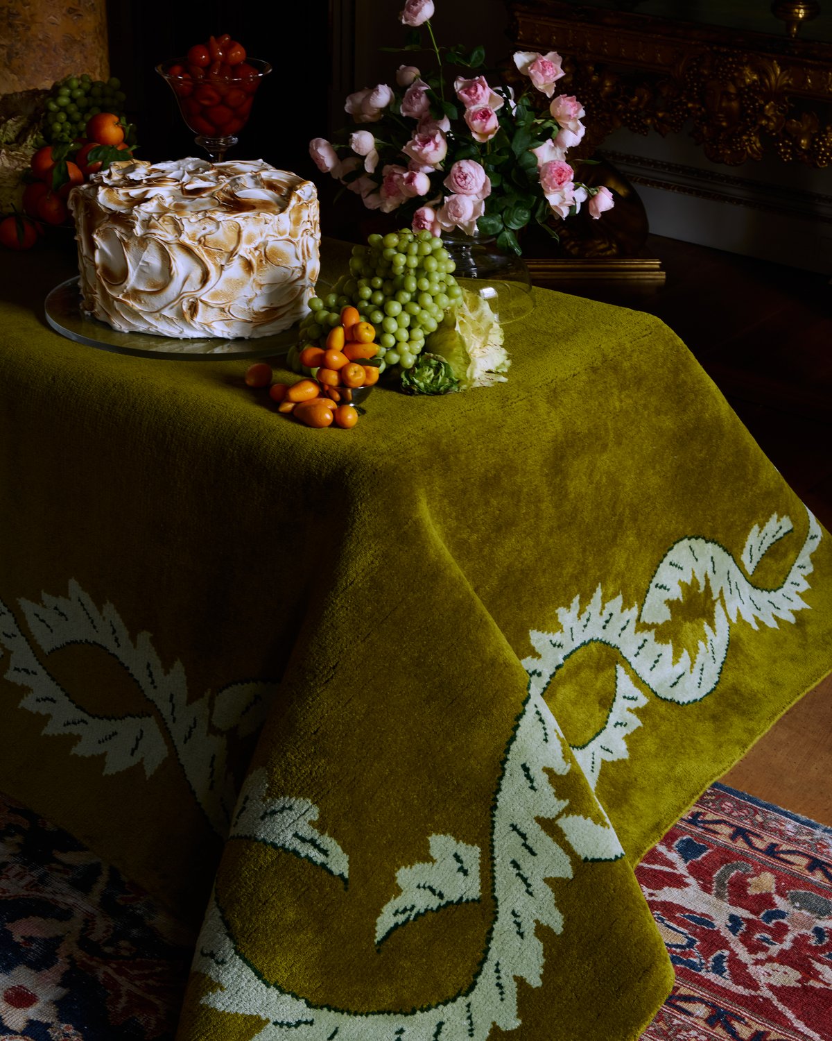 Tapis en laine moelleux Climbing Vine en Olive photographié drapé sur une table avec un gâteau décadent et des fleurs.