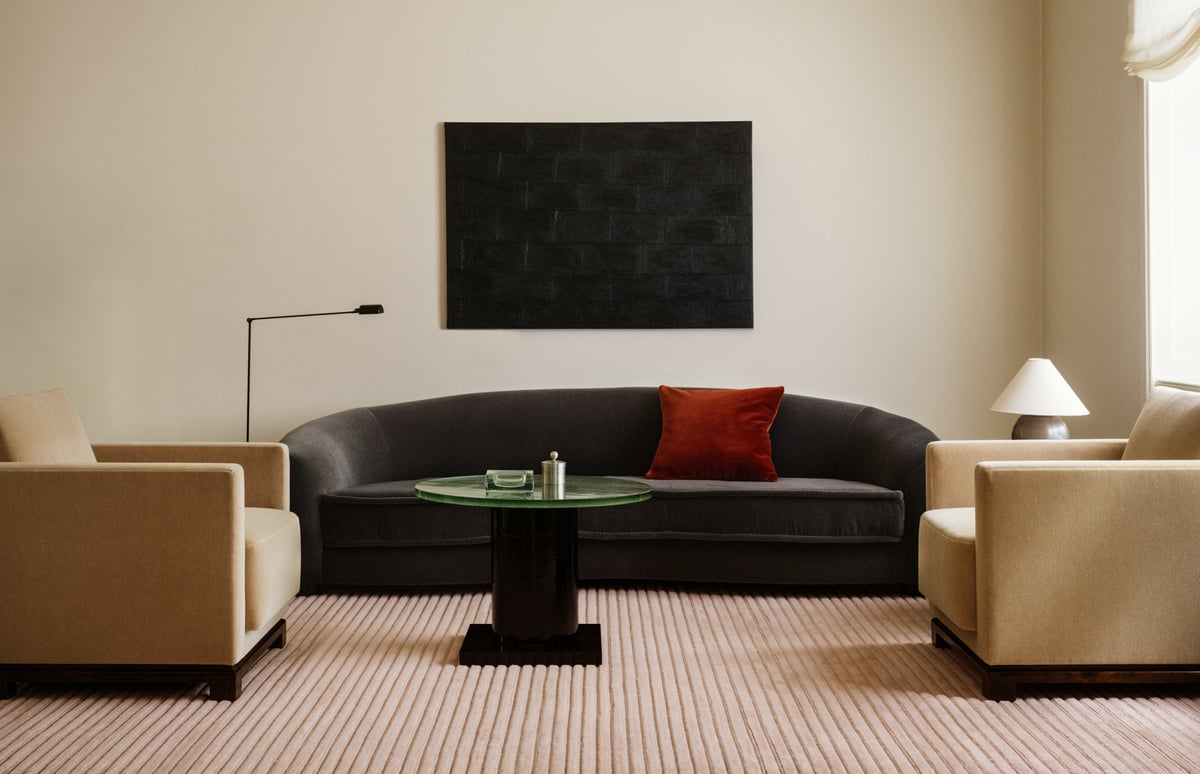 Park 02-matta i Rose – en mjukt rosatonad matta med tonala vertikala ränder, som förankrar ett modernt vardagsrum med skulpturala sittmöbler och ett runt soffbord i glas.