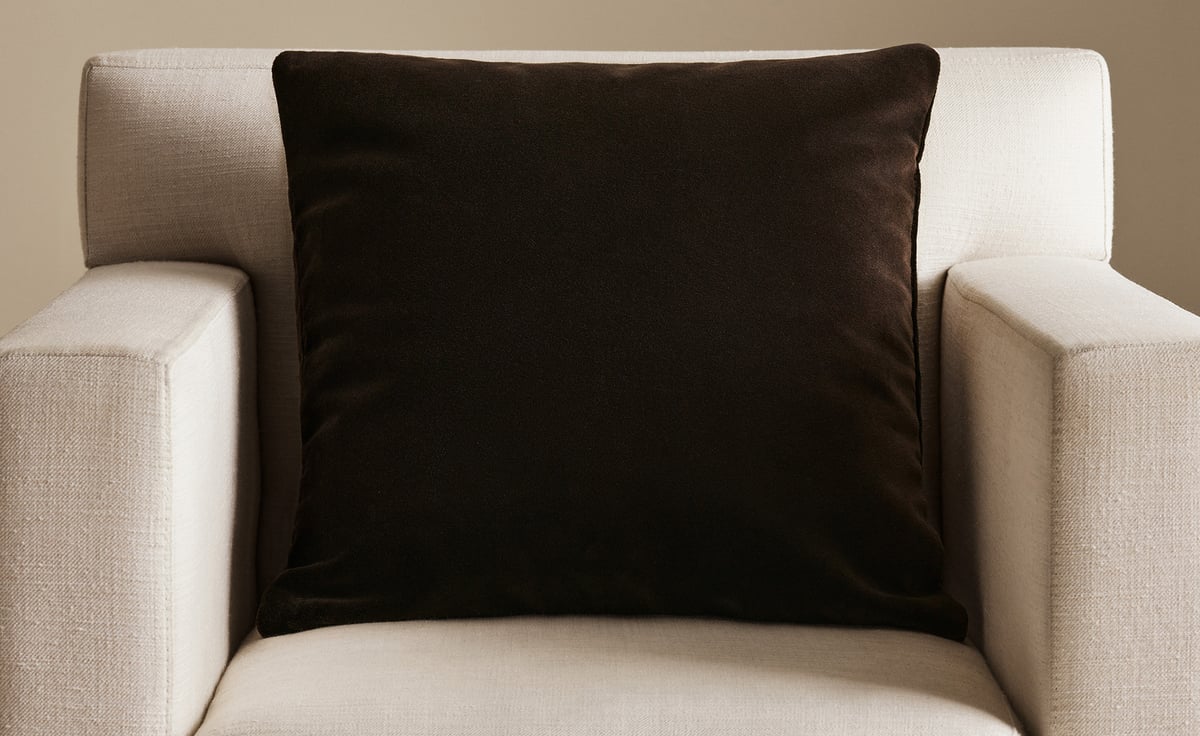 The Teddy Velvet pillow cover in Walnut, photographed on a light upholstered armchair in soft, warm light.