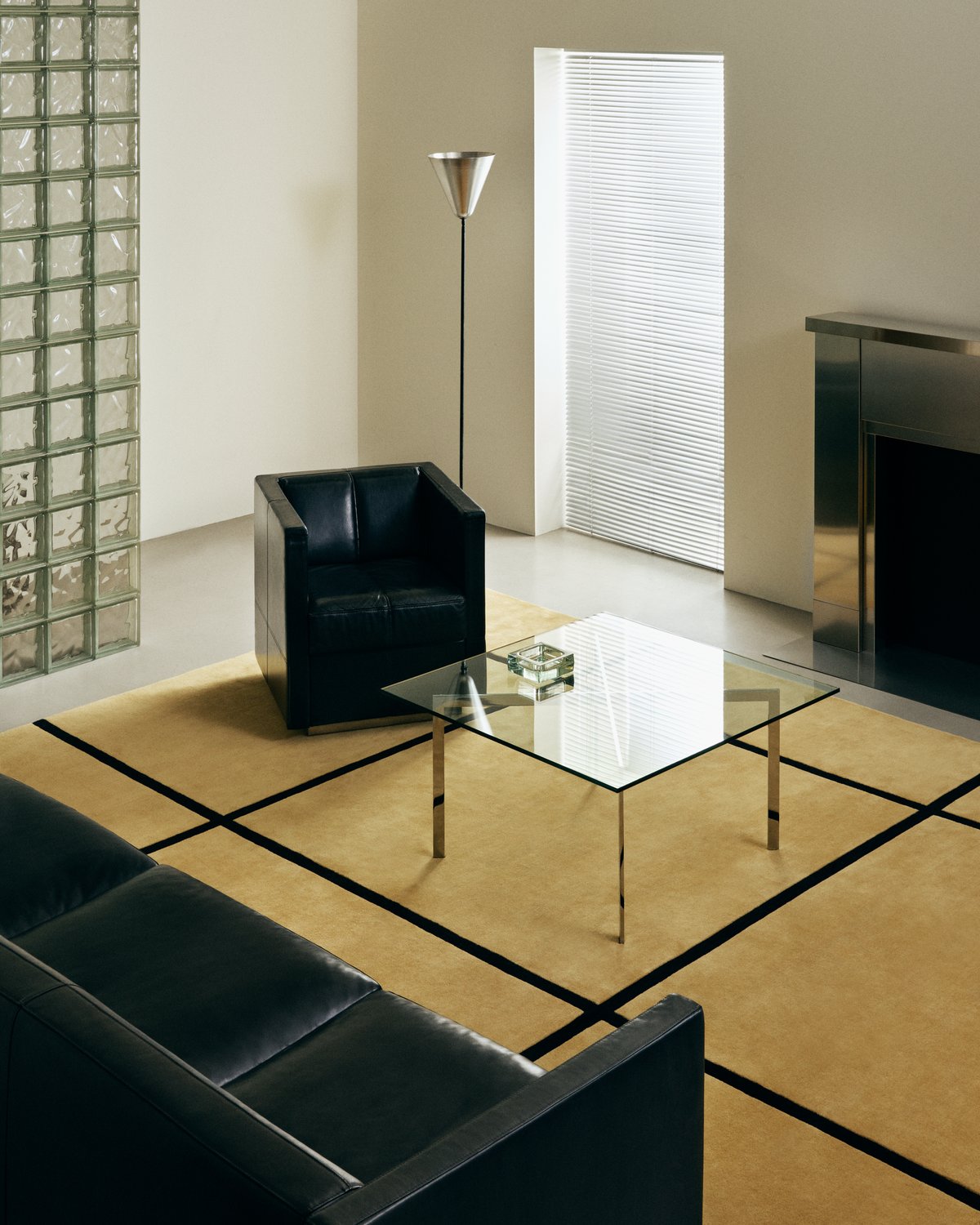 Plush wool rug Pavilion in Yellow pictured in a modern living room with a chrome fireplace, glass coffee table and black leather sofa.