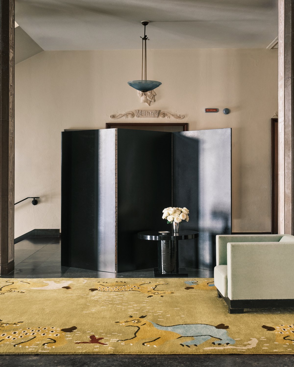 Grace 03 – Fauna — styled inside Stockholm Concert Hall. A golden beige rug with playful animal forms and organic patterns, paired with sculptural furniture and neoclassical details.