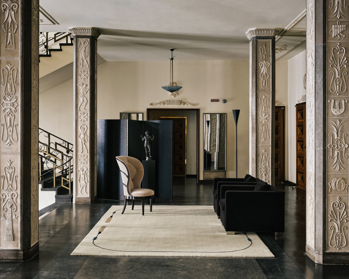 Grace 02 – Tassel — styled inside Stockholm Concert Hall. A handwoven cream rug with subtle tassel-inspired lines, shown with sculptural furniture and neoclassical detailing.