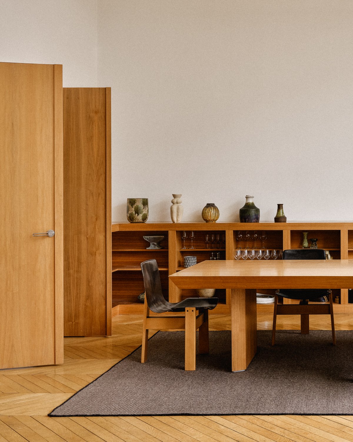 Wool flatweave rug Zero Basket - Brown in a modern dining room with artistic wooden furniture and glassware shelves in Paris.