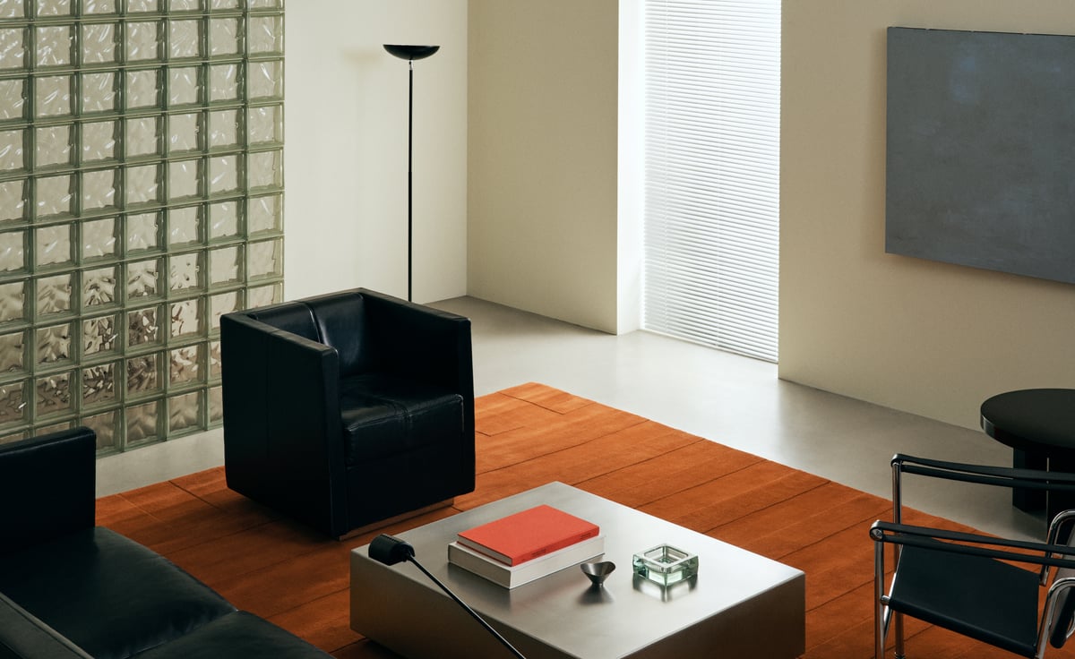 Lux 02 – Burnt Orange brings rich warmth and quiet structure to this modernist space. Its tonal texture grounds sleek black leather seating and brushed metal accents, adding depth and contrast to the minimalist palette.