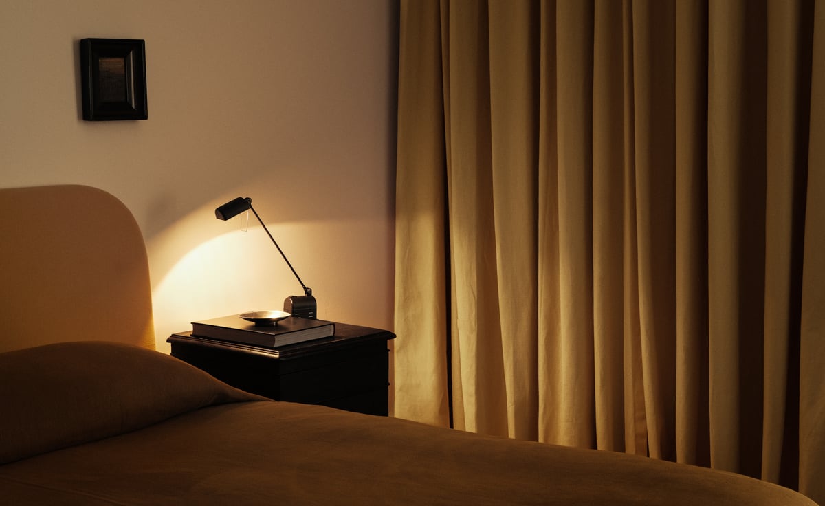 The Blackout curtains in Leo are shown in a softly lit bedroom with matching warm tones, featuring a neatly made bed, dark nightstand, and reading lamp.