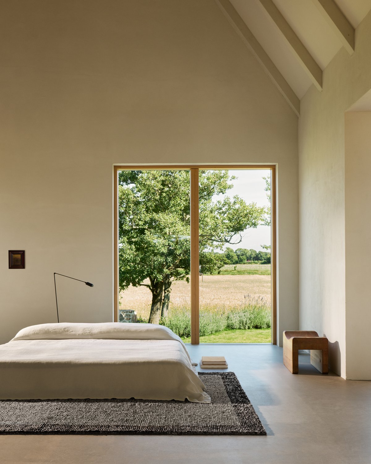 Zotteliger Wollteppich Ryya in Black/White, abgebildet in einem modernen Schlafzimmer mit großen Fenstern mit Blick auf ein Feld.