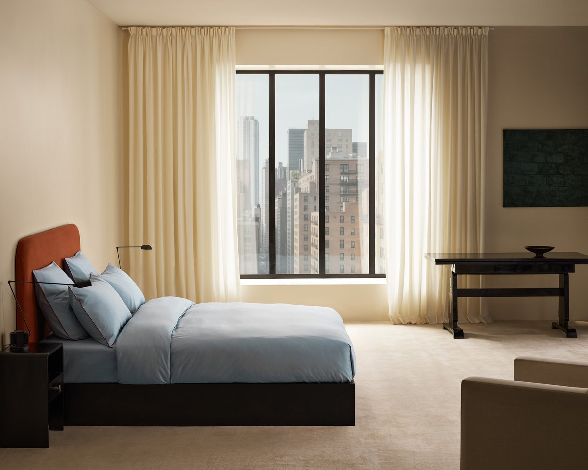 Signature Headboard in Burnt Red with the Percale Duvet Cover in Shirt Blue/Red, photographed in a bright bedroom with sheer curtains and a large window.